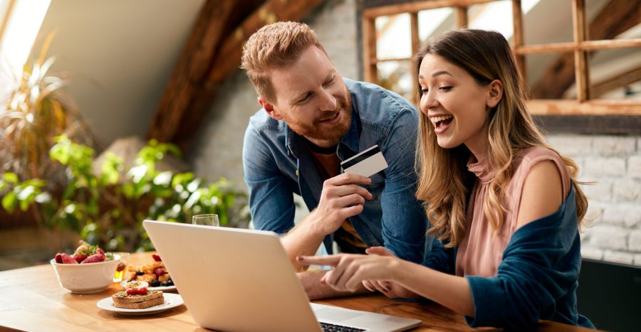Happy couple having fun while online shopping at home. Happy woman pointing on something on laptop screen while shopping on the internet with her husband at home.